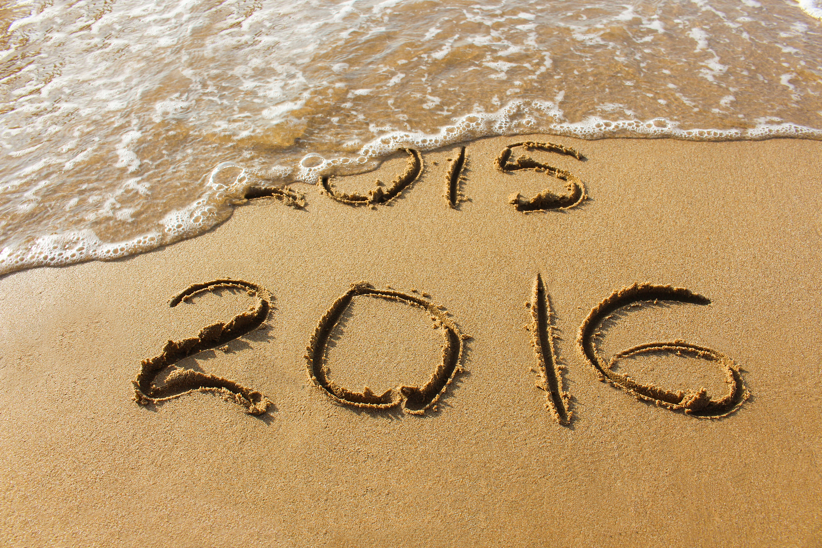 2015 and 2016 year written on sandy beach sea. Wave washes away