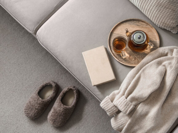 Cashmere sweater, reading and serving tray on gray sofa. Warm weekend at home aesthetics. Detail of cozy winter home interior. Warm soft winter slipper on carpet at home