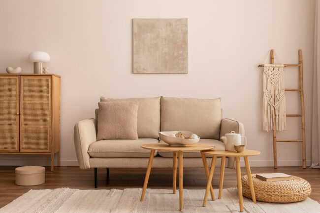 Interior design of cozy living room interior with mock up poster frame, beige sofa, rattan commode, stylish rug, round wooden coffee table, pilows in ball and personal accessories. Home decor. Possible investment property.
