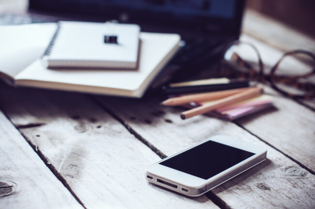Hipster home office tabletop: papers and notebooks, reading glasses, smart phone, pen on an old wooden board background. Vintage lifestyle of a realtor reading books to help their career