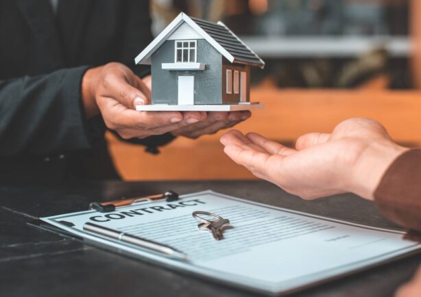 Home seller holding a model home pasing it to a trusted realtor to help sell. Underneath a contract and keys. Niche Real Estate Website